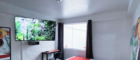 Camera d'albergo con due letti, una scrivania, una sedia, una televisione e una finestra con tende.