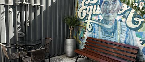 A patio area with a metal fence, a table with chairs, a bench, and a colorful mural on the wall.