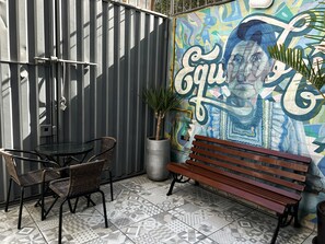 A patio area with a metal fence, a table with chairs, a bench, and a colorful mural on the wall. - Magdalen House (Lima)