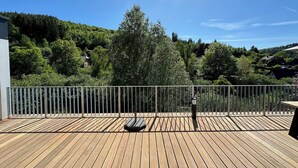 Une terrasse en bois avec une rambarde en métal, offrant une vue sur une colline boisée.