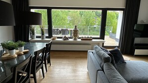 Un salon moderne avec un coin repas, de grandes fenêtres et une vue sur la verdure environnante.