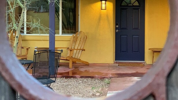 Un edificio amarillo con una puerta azul oscuro, una silla de madera y una mesa afuera.