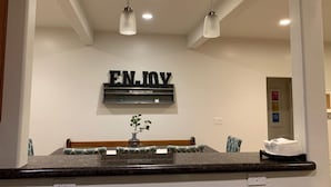 Zona de recepción de hotel con un gran letrero que dice 'ENJOY', una planta pequeña y un mostrador con un perchero para toallas.
