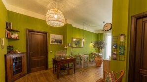 Ein Zimmer mit Schreibtisch aus Holz, einem Korbstuhl, einem Bücherregal und einem großen Spiegel an der Wand.