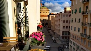 Ein Balkon mit Blumentöpfen, Blick auf eine Straße mit parkenden Autos und ein Gebäude mit einer Kuppel im Hintergrund.