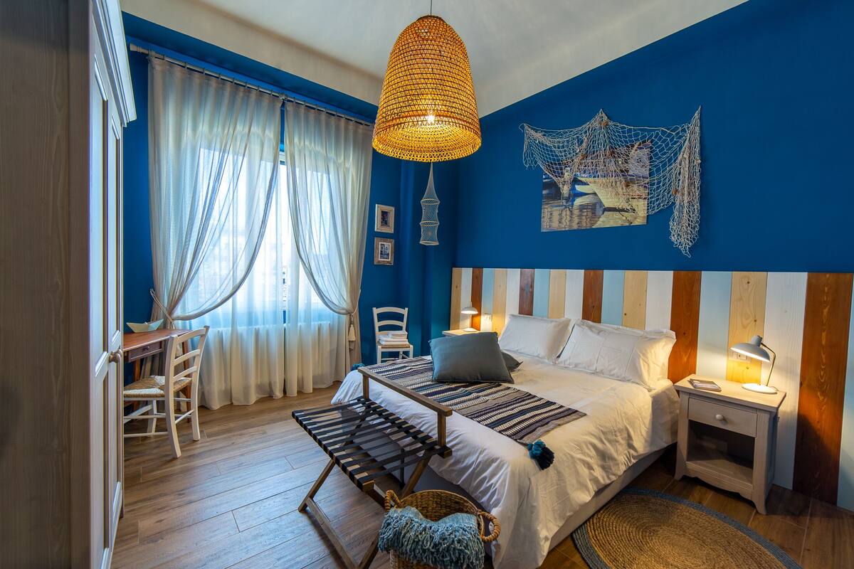 Quarto com cama, mesas de cabeceira, escrivaninha e uma cadeira.