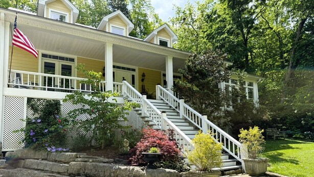 A two-story house with a porch, a flag, and a staircase leading to the entrance. - Bourbon Estate  sleeps 12, 6 BRs, 47ac of Waterfalls, Meadows and Creek (Bardstown)