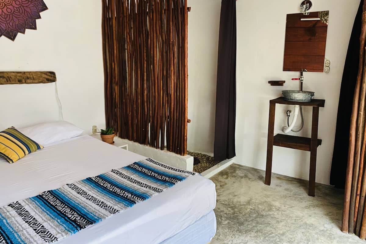 Un dormitorio con cama, un separador de madera, un lavamanos pequeño y un espejo.