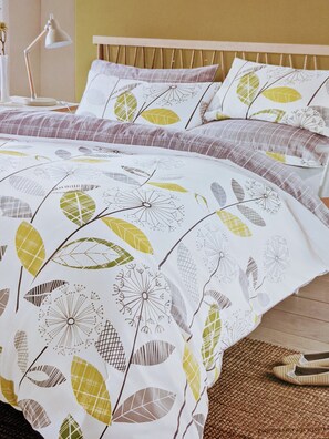 A bed with a patterned bedspread, a bedside lamp, and a woven rug.