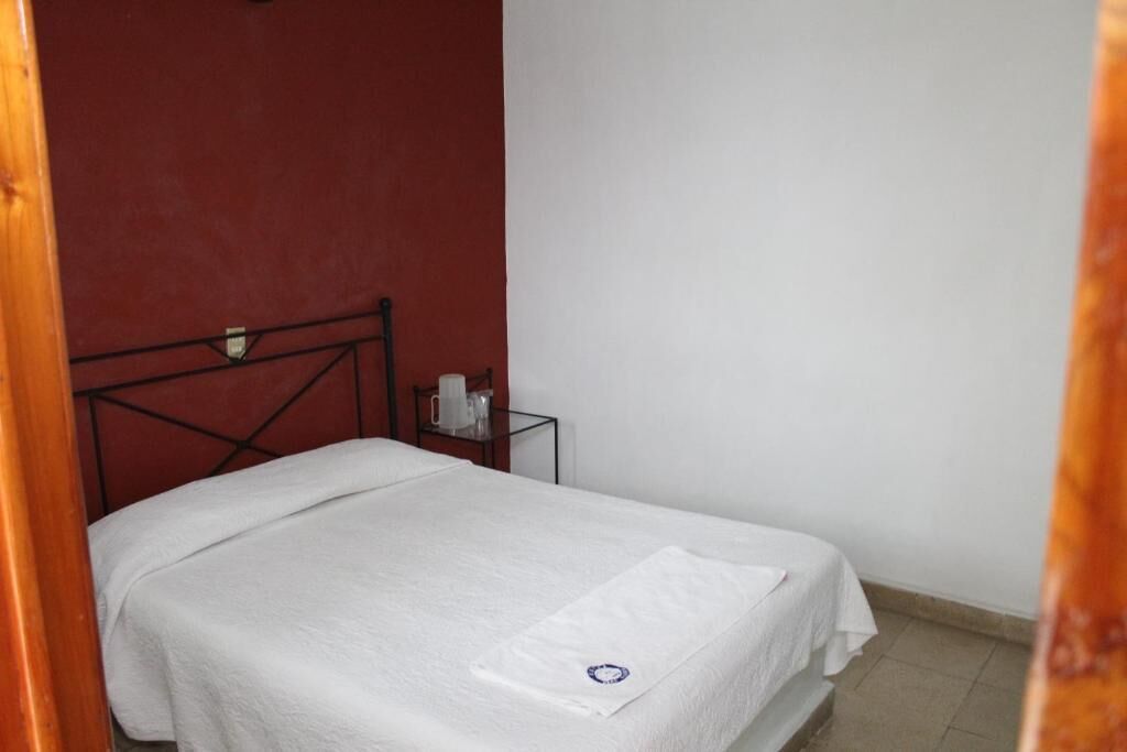 Una cama pequeña y ordenada en una habitación con pared roja y marco de puerta blanco.