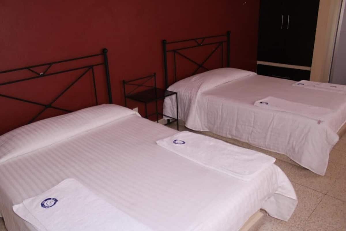 Two single beds with metal frames in a room with a red wall and a wardrobe.