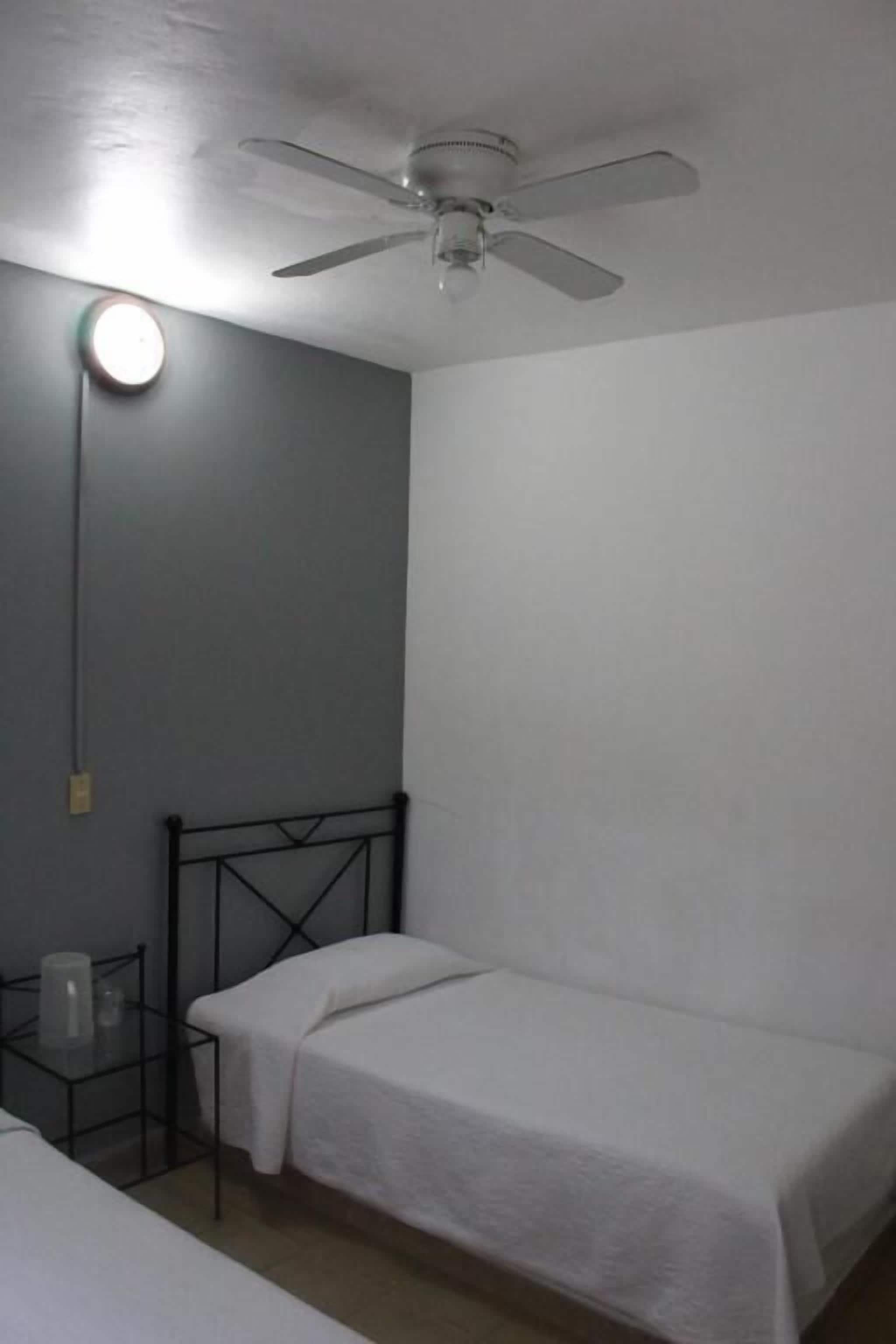 A single-bed room with a ceiling fan, a bedside table, and a nightstand.