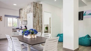 A modern kitchen with white cabinets, a wooden accent wall, and a dining area with white chairs and a table. - Villa Conchita Torremolinos (Torremolinos)