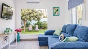 A modern living room with a blue sofa, a small table with a vase of flowers, and a view of a garden through a large window. - Villa Conchita Torremolinos (Torremolinos)