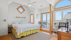 A bedroom with a bed, a desk, a chair, a balcony, and a view of the ocean. - Blue Pointe Bayside | Cul-de-Sac Waterfront w/ 4 Decks, Screened Porch, Sunsets & Bay Views (Chincoteague Island)