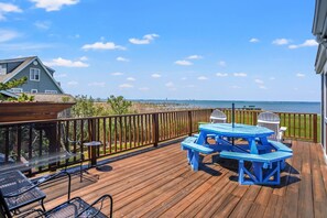 Une terrasse en bois avec une table de pique-nique et des chaises bleues, donnant sur une plage.