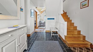 A hallway with a white dresser, a mirror, a wooden staircase, and a chair. - Blue Pointe Bayside | Cul-de-Sac Waterfront w/ 4 Decks, Screened Porch, Sunsets & Bay Views (Chincoteague Island)