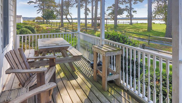 A wooden deck with a table and chairs, overlooking a grassy area with trees and a body of water. - Channel Lookout | Memorial Park Water Views w/ Private Deck, Assateague Channel Scenery & Fishing (Chincoteague Island)