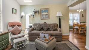Ein gemütliches Wohnzimmer mit einer Couch, Hocker und Sesseln, ein Essbereich mit Tisch und Stühlen sowie ein Oberlicht.