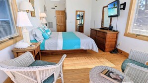 A bedroom with a bed, wooden dresser, television, wicker chairs, and a ceiling fan. - Grey Heron | Waterfront Home w/ Dock, Kayak Launch, Screened Porch, Epic Sunsets & Pet Friendly (Chincoteague Island)