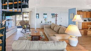 A spacious living room with a high ceiling, a staircase, a sofa, a coffee table, and a lamp. - Grey Heron | Waterfront Home w/ Dock, Kayak Launch, Screened Porch, Epic Sunsets & Pet Friendly (Chincoteague Island)