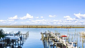 A marina with boats docked at wooden piers, a clear sky, and a distant bridge. - Sunset Bay Villa 212 | Waterfront Balcony + Pool + Walk to Downtown + Pet Friendly (Chincoteague Island)