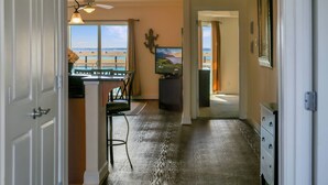 A hallway with a view of the beach, a dining area with a table and chairs, and a dresser with drawers. - Sunset Bay Villa 212 | Waterfront Balcony + Pool + Walk to Downtown + Pet Friendly (Chincoteague Island)