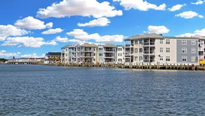 A waterfront hotel with multiple floors, balconies, and a dock extending into the water. - Sunset Bay Villa 212 | Waterfront Balcony + Pool + Walk to Downtown + Pet Friendly (Chincoteague Island)