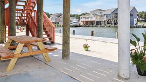Una terraza de madera con una mesa de picnic, una escalera y vistas a casas y un barco amarrado al agua.