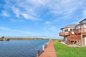 A waterfront property with a wooden dock leading to a house with a balcony.