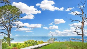 Une promenade en bois mène à une plage d’où l’on a une vue dégagée sur l’océan, et une jetée en bois s’avance dans l’eau.