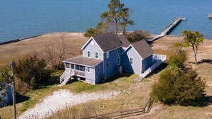 Une maison à deux étages avec un porche et une jetée qui s’avance dans un plan d’eau.