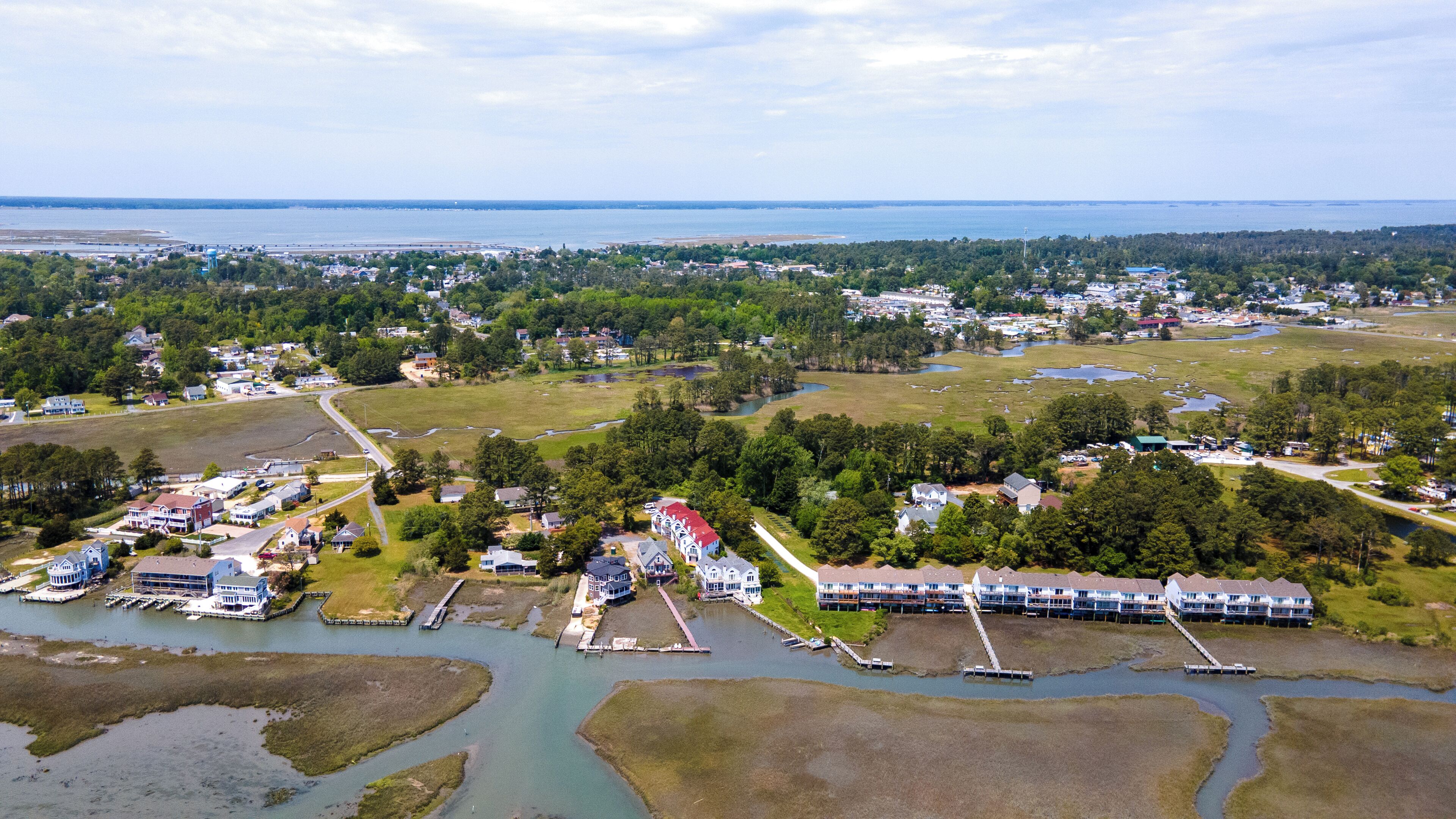 Vista aérea de un pueblo costero con zonas residenciales, un puerto deportivo y un puente que lo conecta al continente.