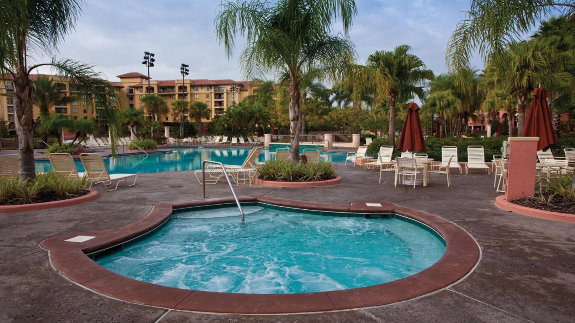 Zona de piscina de hotel con jacuzzi, sillas de descanso y palmeras.