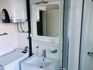 Een moderne badkamer met een ingebouwde wasmachine, een wastafel, een spiegel en een douchecabine van glas.