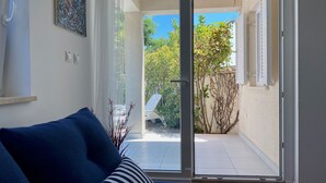 Una habitación con un sofá azul, un ventanal corredero que da a un balcón con vistas a zonas verdes y una pared blanca con un cuadro.