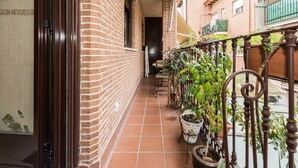 Un balcon étroit avec un mur en briques, des plantes en pot et une rambarde en métal.