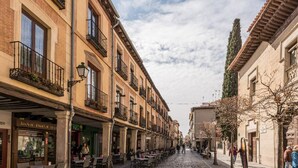 Une rue pavée bordée de bâtiments traditionnels, avec des terrasses de café et un ciel dégagé.