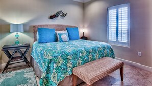 A bedroom with a bed, a bench, a nightstand, a lamp, a decorative wall piece, and a window with blinds. - 5th floor, Gulf views, 2 Pools, Free Beach Service, Garage Parking (Miramar Beach)