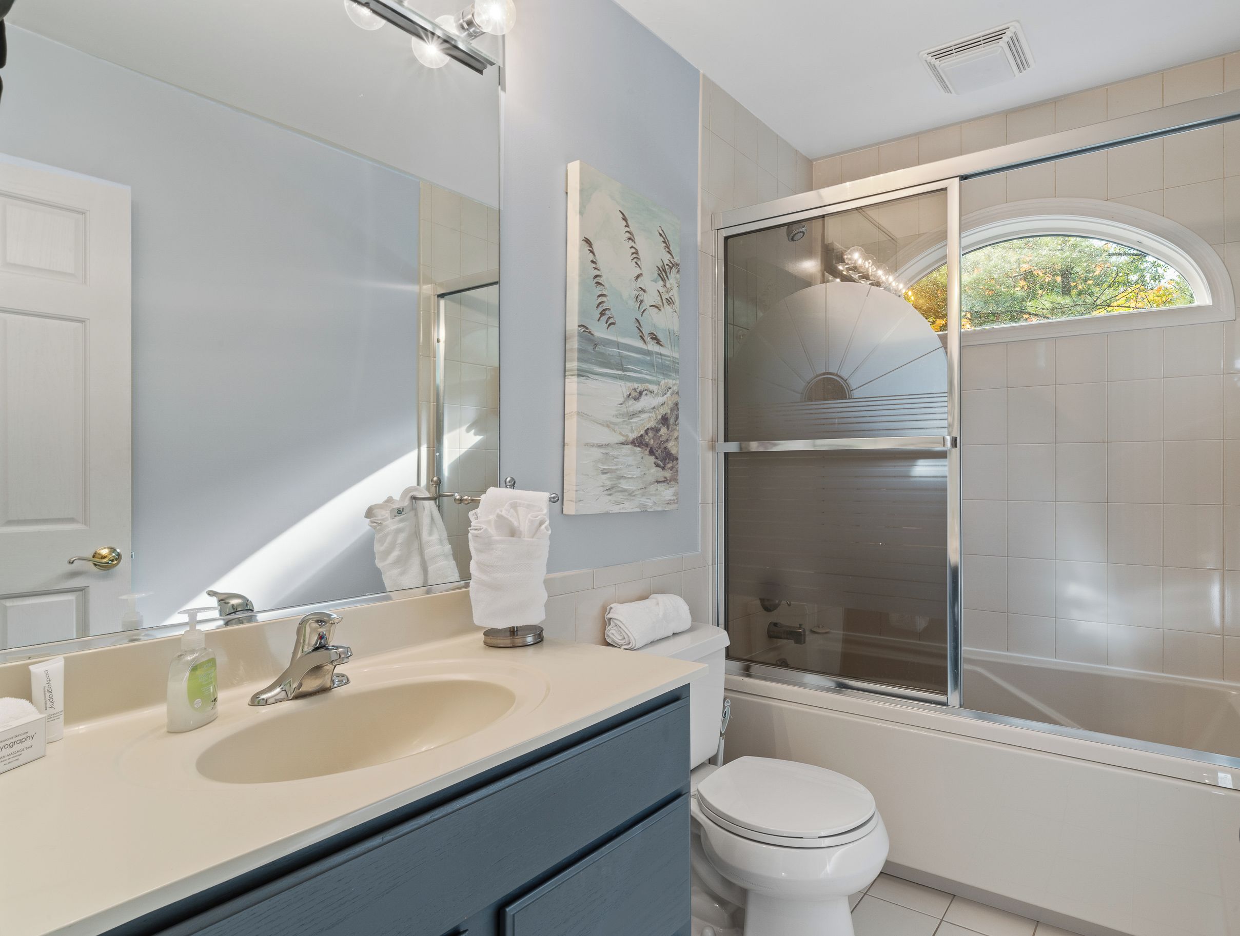 A modern bathroom with a large mirror, a sink, a toilet, and a glass-enclosed shower.