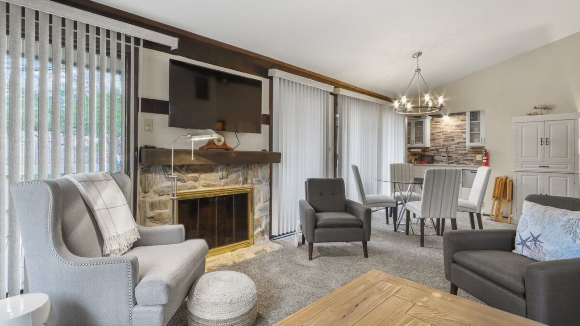 A modern living room with a stone fireplace, grey sofas, and a dining area with a chandelier.