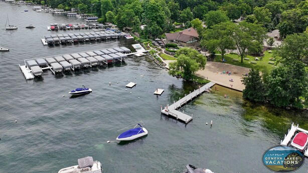 An aerial view of a lakeside property with docked boats, a marina, and a beach area with picnic tables. - Sail Away @ Abbey Springs |Golf Cart |Golf Course |Wooded View |Wraparound Deck |Pool |Tennis |Beach (Fontana)