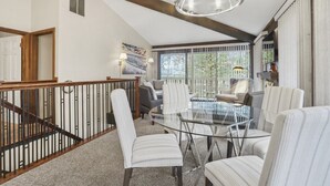 A spacious dining area with a glass table and striped chairs, a chandelier, and a view through large windows. - Sail Away @ Abbey Springs |Golf Cart |Golf Course |Wooded View |Wraparound Deck |Pool |Tennis |Beach (Fontana)