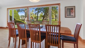 A dining area with a large table and chairs, large windows with a view of a park, and a framed picture on the wall. - Lake Benedict Lakefront Home with Fire Pit Large Yard Kayak Friendly (Genoa City)