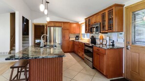 A kitchen with wooden cabinets, a granite countertop, stainless steel appliances, and a bar stool. - Lake Benedict Lakefront Home with Fire Pit Large Yard Kayak Friendly (Genoa City)