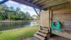 Une structure en bois offrant une vue sur une étendue d’eau, des marches menant à une porte et un tuyau d’arrosage vert accroché au mur.