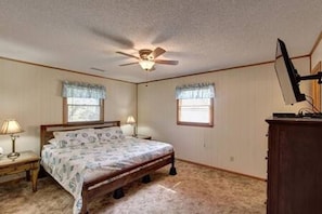 A bedroom with a bed, two bedside lamps, a ceiling fan, and a dresser.