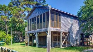 Un bâtiment rustique en bois, doté d’une grande fenêtre en verre, entouré d’arbres et bordé par un plan d’eau.