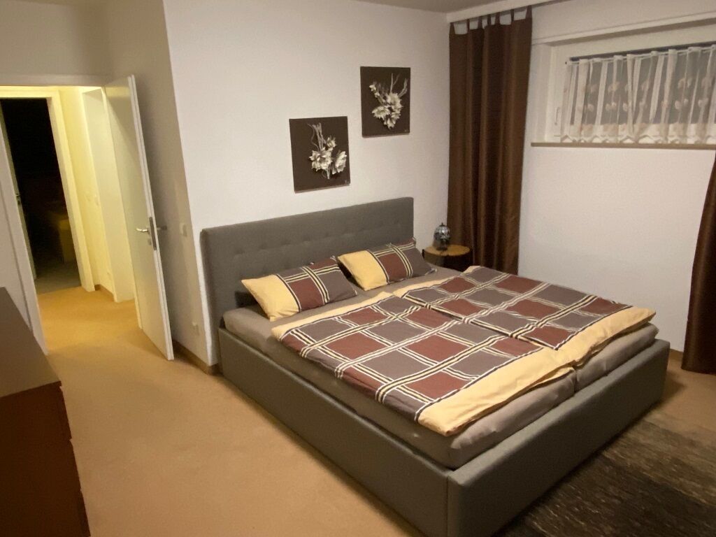 A bedroom with a bed, a nightstand, and a window with curtains.