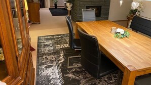 Un coin repas avec une table en bois, des chaises noires, une cheminée en pierre et un tapis à motifs.